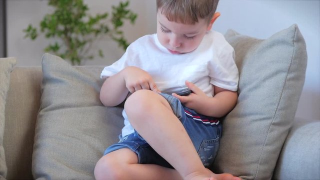 Child tech addiction concept play game at home. Little Boy preschool child using a digital tablet technology device looks telephone.Plays in the phone sitting on the sofa alone.