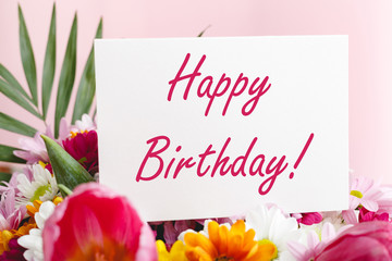 Happy birthday text on card in flower bouquet on pink background. Flower delivery, congratulation...