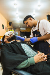 Young Latin Barber At Work In Stylish Barbershop. Cool, bearded man enjoys the moment.