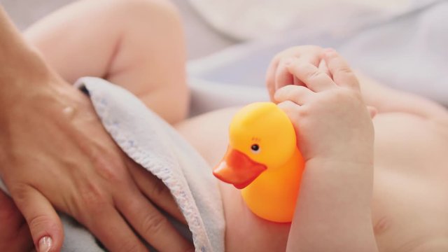 Mother hand drying baby skin with the towel after the bath. Baby holding duck toy.