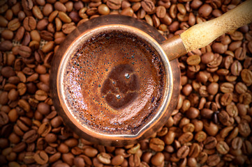 traditional turkish coffee in copper coffee pot on coffee beans, hot drink concept