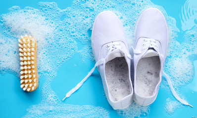 Sneakers with foam of powder detergent water dissolution and wooden brush on blue background....