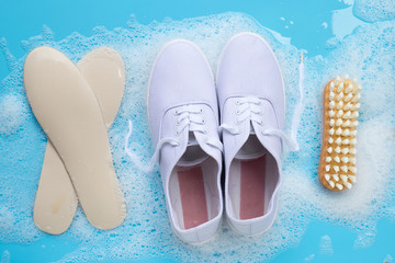 Sneakers with foam of powder detergent water dissolution and wooden brush on blue background.