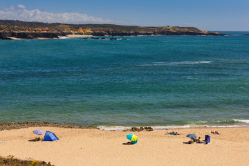 Fototapeta na wymiar People bathing at the beach in Vila Nova de Milfontes, on hot summer day, blue sky, crystalline water