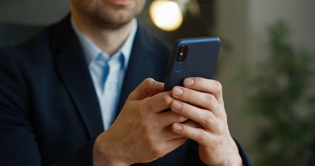 Close up of smartphone in hands. Businessman tapping and scrolling on mobile phone in office.