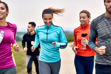 Happy athletic woman running marathon with her friends in nature.