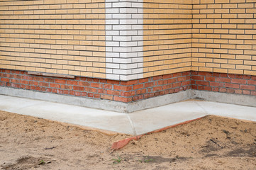 Corner of new brick house faced by decorative brick tile and with concrete blind area