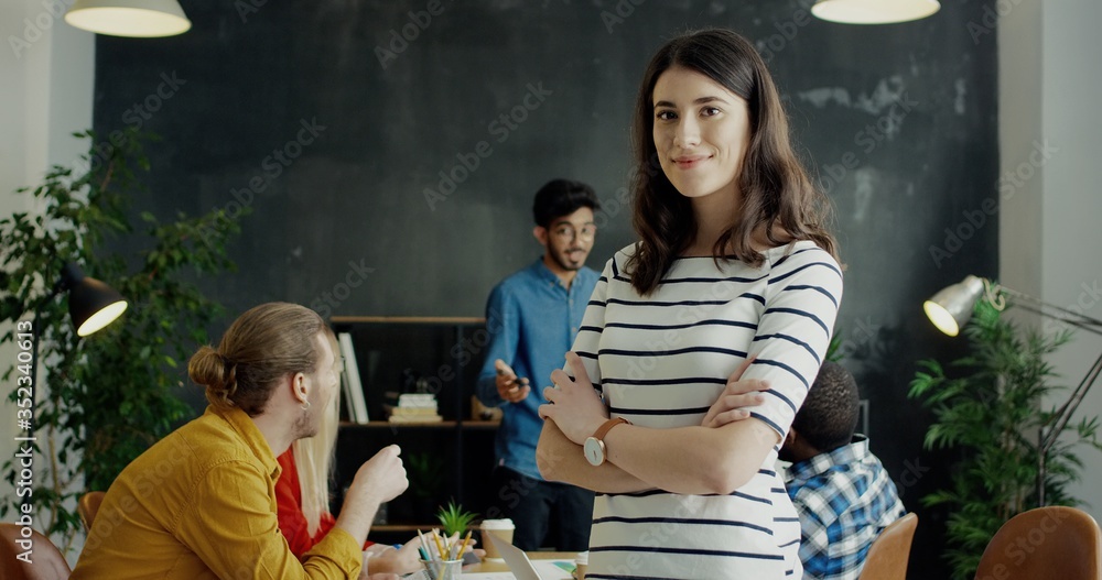 Wall mural portrait of pretty young cheerful girl turning face to camera and smiling. team of startuppers on ba