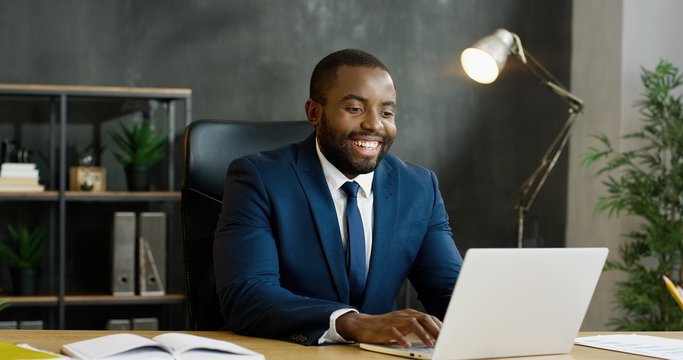 African American businessman sitting at table and having videochat on laptop computer.