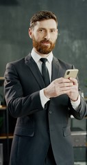 Portrait of Caucasian joyful businessman in office texting message on smartphone.