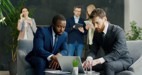 Mixed-races handsome businessmen sitting at meeting at laptop computer and discussing some project....