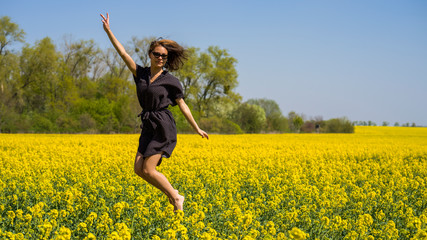Eine junge Frau springt in einem Rapsfeld in die Luft