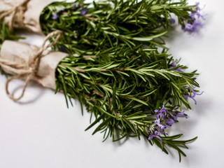 Two bunches of fresh rosemary wrapped in paper and tied with jute twine lie on a white  background. Blooming rosemary. Close-up. Fragrant spice. Nature background.