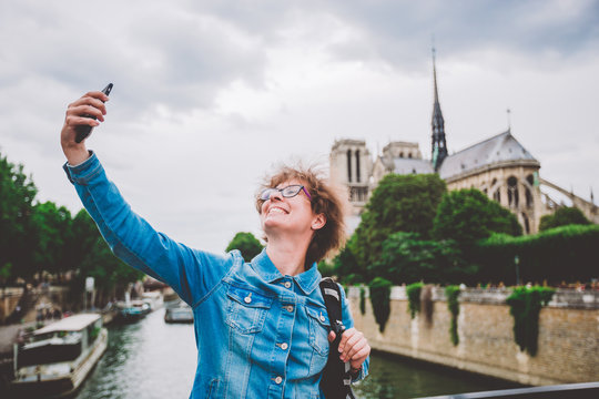 Caucasian female tourist photographing themselves by mobile telfon on background Notre Dame Cathedral from bridge over Seine bridge arsheveshe. Image Cathedral of Notre Dame de Paris