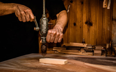 carpenter drilling a wooden plank with an ancient mechanical hand drill in atelier, closeup.