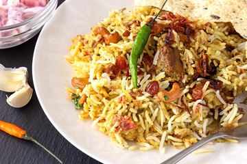 Halal Indian chicken or mutton Biryani served with yogurt tomato raita over white background. Selective focus.