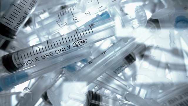 A lot of new plastic disposable syringes falling onto a transparent surface. Closeup. Shallow depth of field. Slow mo, slo mo, slow motion, high speed camera
