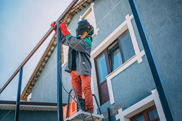 A welder welds a metal pole with electric welding, holds an electrode in his hands