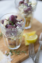 Feta and black olive appetizer with lemon and thyme in a glass on wood surface