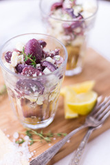 Feta and black olive appetizer with lemon and thyme in a glass on wood surface