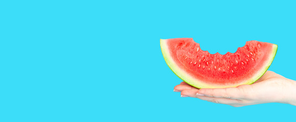 A woman hand holding a slice of watermelon on a blue background. Long banner