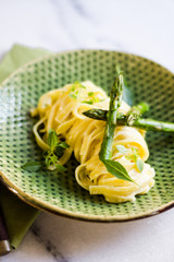 Pasta with asparagus and basil on a green ceramic and white surface