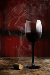 copa de vino tinto sobe mesa rustica de madera y fondo rojo  con humo 