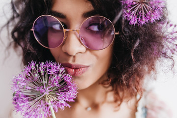 Close-up shot of lovable black girl playfully looking away. Studio portrait of blithesome curly lady posing with purple flowers.