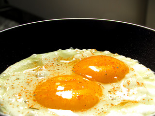 Two fried eggs seasoned with spices in the frying pan