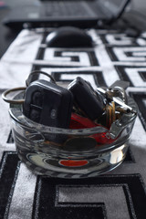 Glass bowl with various small objects on the home desk. Things like keys, coins, buttons, and other house small objects. Close up, selective focus