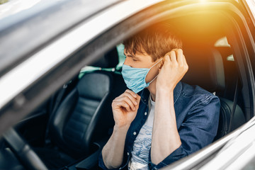 A man in a protective medical mask, sitting behind the wheel of a car. Quarantine, coronavirus