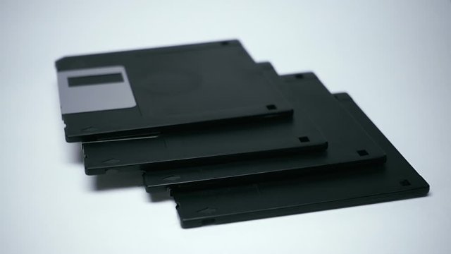 Old vintage black floppy diskettes are falling to a white surface. Closeup. Shallow depth of field. Slow motion. High speed camera