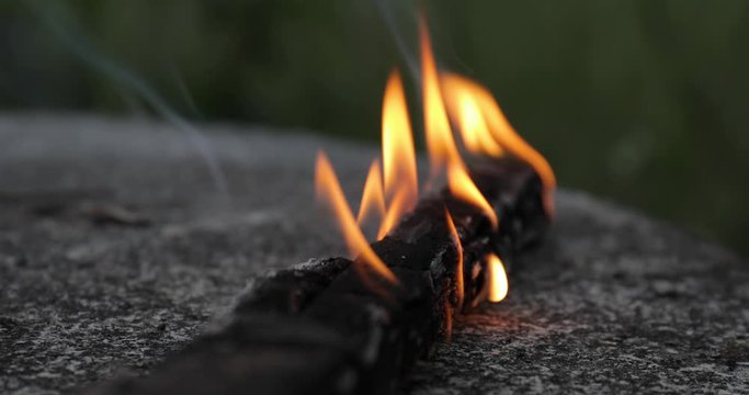 Campfire, playing with fire burning a single stick of wood flaming