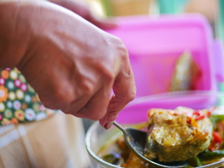 The woman`s hand scoops up a spoon from a bowl of fish soup.