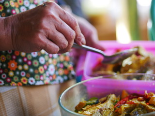 The woman`s hand scoops up a spoon from a bowl of fish soup.