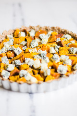 Fototapeta na wymiar Pumpkin and blue cheese quiche with herbs on a marble surface and rustic napkin