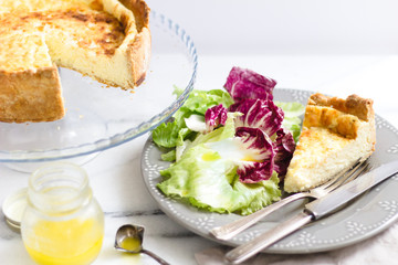 Quiche with colorful salad and dressing on a marble surface