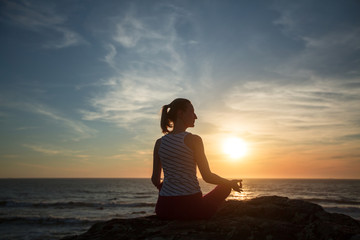 Silhouette of yoga woman meditation on the ocean beach at fantastic sunset.