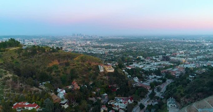 Aerial, tilt down, drone shot of the Hollywood cityscape, revealing the quiet Laurel canyon boulevard, Downtown Los Angeles skyline in the background, during dusk, in California, USA