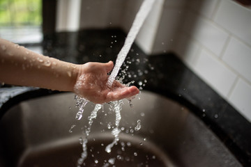 Cropped image of child washing his hands. Water splashes all around. Virus spread prevention