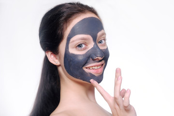 Teenager girl in a black mask, natural photo of a real mask on a young girl. Texture dark cream. Model on a white background smokes skin