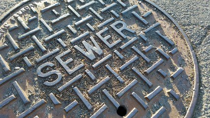 Extreme closeup of metal sewer cap on a dry, cracking road during summer
