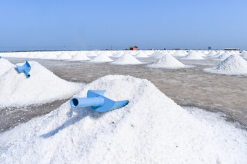White sea salt is scooped up into piles like mountains and dried in the sun. Behind is a clear blue...