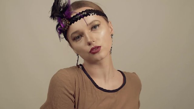 Girl in the 90s style, chicago style. Hat, headband with decorative feathers on the head. Incredible jewelry, long earrings with diamonds, coquette. dance and pouse