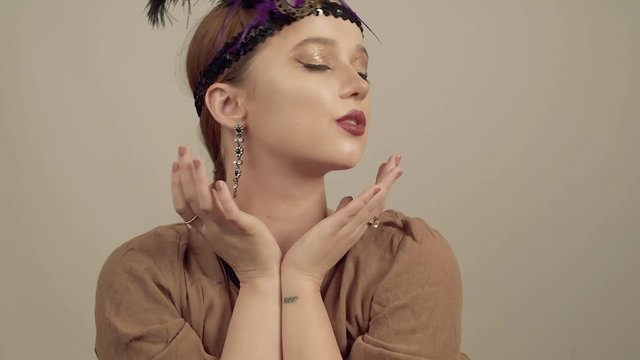 Girl in the 90s style, chicago style. Hat, headband with decorative feathers on the head. Incredible jewelry, long earrings with diamonds, coquette.