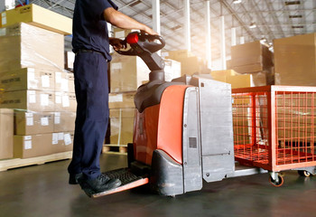 Motion blur of worker driving electric forklift pallet jack unloading pallet goods, Interior of...