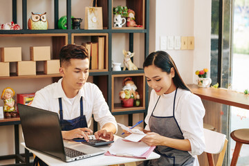 Young cafe owners sitting at table, checking bills and paying online