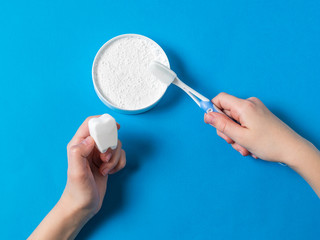 The child is holding a figurine of a tooth and a brush with tooth powder.