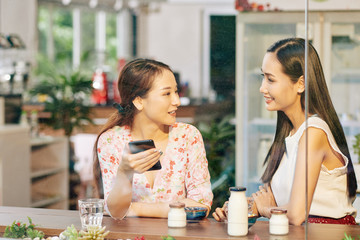 Beautiful young Asian female friends having breakfast at cafe table and discussing latest news and gossips