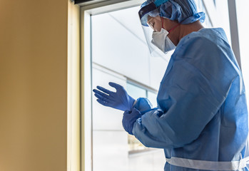 A respiratory therapist prepares to see a patient with influenza but putting on gloves and other protective gear.